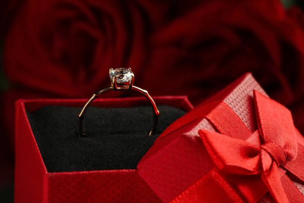 istock Beautiful engagement ring with gemstone in box against roses, closeup 1398267406