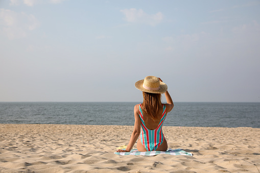 Woman with beach towel resting on sandy seashore, back view. Space for text