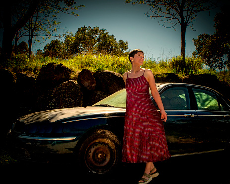 A woman in a dress in front of an old abandoned car