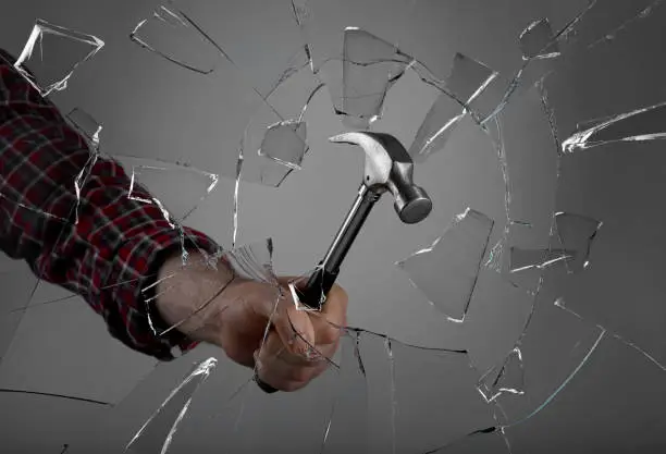 Photo of Man breaking window with hammer on dark grey background, closeup