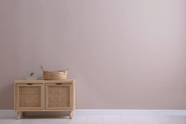 armário de madeira com relógio e cesto de vime perto da parede bege, espaço para texto. design de interiores - wicker drawers - fotografias e filmes do acervo