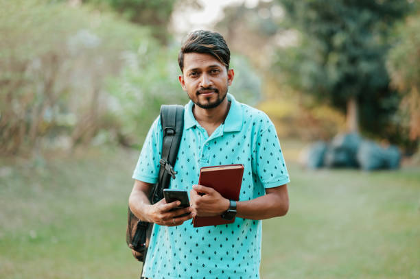 istock Young male student using smartphone with backpack and books at park 1398271349