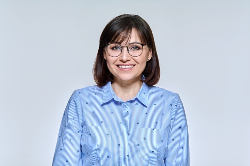 Portrait of confident positive mature businesswoman looking at camera on light studio background. Smiling middle aged female wearing glasses blue shirt. Business professions, work, people 40s concept