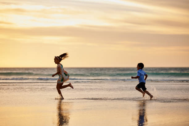 снимок маленького мальчика и девочки, играющих в погоню на пляже - dark little girls child happiness стоковые фото и изображения
