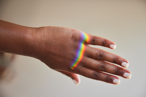 Close-up of a ray of rainbow colored light refracting onto a the hand of woman