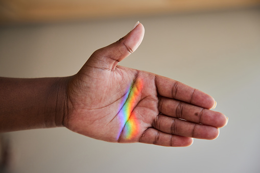 Close-up of a ray of rainbow colored light refracting onto a the palm of woman's hand
