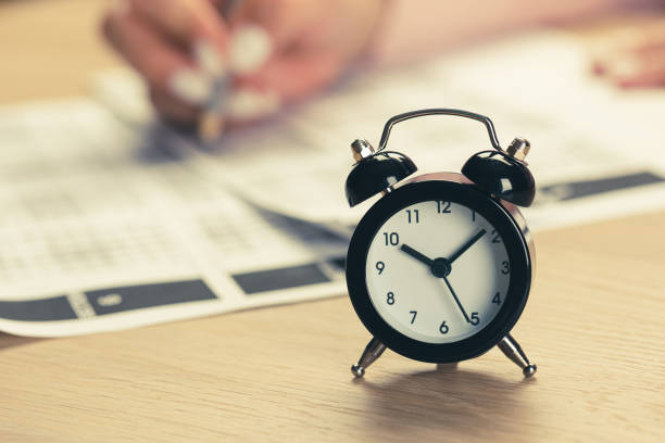 istock alarm clock with time running out. Students hands to take exams, write examination room with pencil holding on optical form of standardized test with answers 1398281060