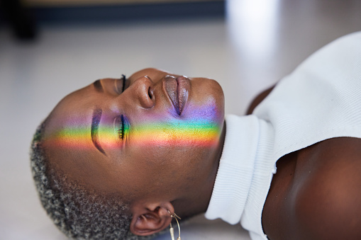 Close-up of a ray of rainbow colored light refracting onto a the face of a woman lying on a floor with her eyes closed