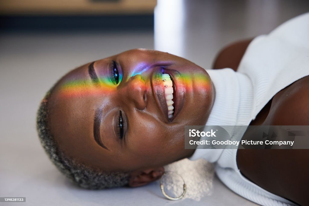 Rainbow colored light refracting onto the face of a smiling woman Close-up of a ray of rainbow colored light refracting onto a the face of a woman lying on a floor and smiling Prism Stock Photo