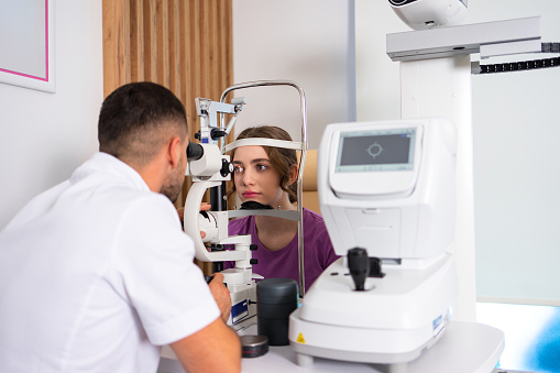 A young male doctor ophthalmologist checks the eye vision of a teenage girl in a modern clinic.