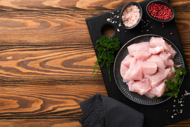 Raw chicken breast sliced or cut pieces on wooden cutting board with herbs and spices on old wooden table background. Raw chicken meat. Top view with copy space. Mock up. stock photo