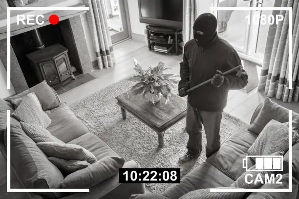CCTV surveillance security camera of burglar breaking into home via back door window with crowbar house robbery concept