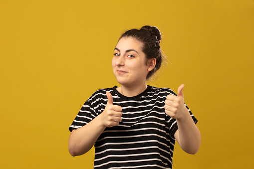 Good Job. Happy Cheerful  Woman Showing Thumbs Up At Camera. Striped t-shirt  on yellow background