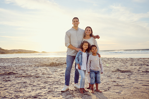 Portrait of a happy mixed race family standing together on the beach. Parents spending time with their cute son and daughter while on holiday. Little siblings playing with their parents on vacation