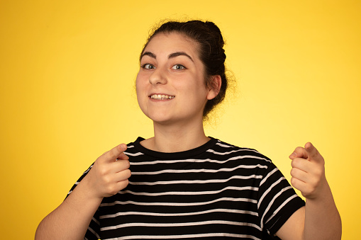 You Got Me. Hey you. Portrait of a woman pointing finger at camera  wearing a striped t-shirt on a yellow background.