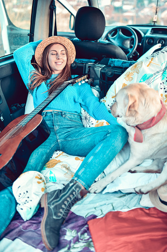 Cute Female Lying Down In Minivan Trunk With Guitar And Dog