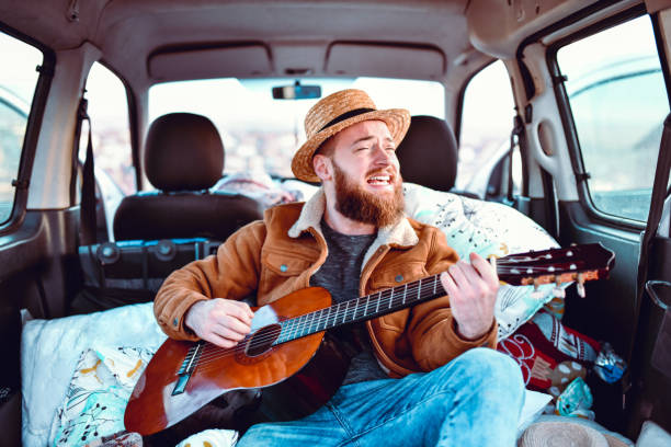 istock Male Smiling And Singing While Playing Guitar In Minivan Trunk 1398299674