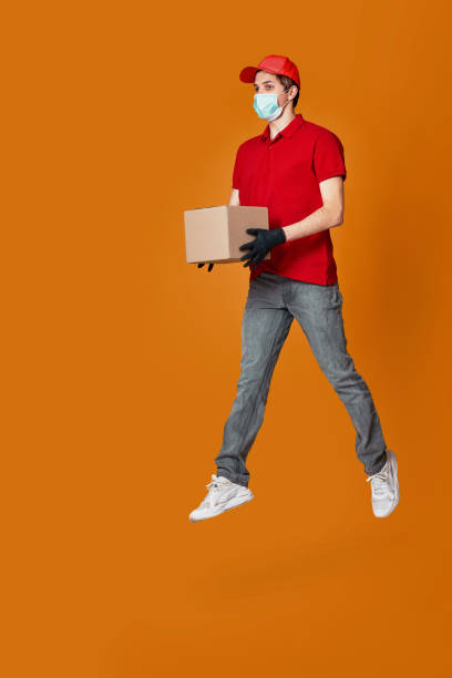 istock Delivery man in face mask holding cardboard box and jumping 1398301263