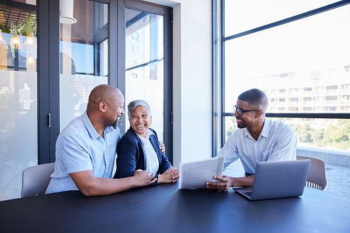 Mature couple smiling while going over documents with their financial advisor during a meeting together at table in his office