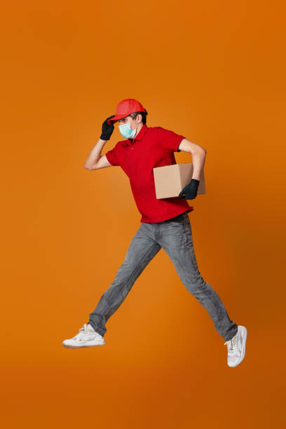 istock Delivery man in face mask holding cardboard box and jumping 1398301284