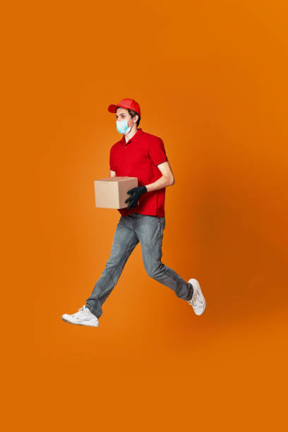 istock Delivery man in face mask holding cardboard box and jumping 1398301289