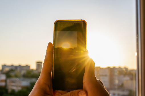 Woman hands holding a mobile phone at sunset golden hour and taking picture