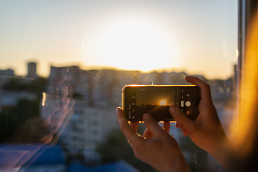 Woman hands taking sunset picture with the mobile phone from the window of a skyscraper