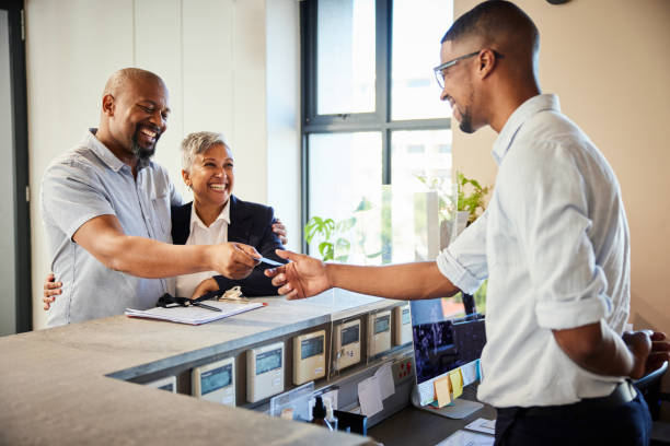 Smiling mature couple giving hotel reception their cardkey Smiling mature couple giving a cardkey to a concierge at the reception desk of a hotel during checkout concierge service stock pictures, royalty-free photos & images