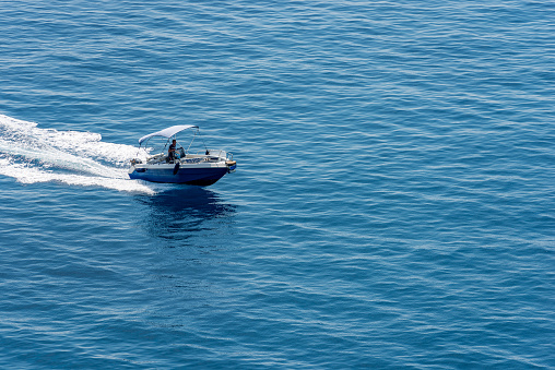 Vernazza, Italy - July 22th, 2019: Small blue motor boat with one person on board runs fast in the blue Mediterranean sea with white wake, photographed from above. Cinque Terre, Liguria, Italia, southern Europe.
