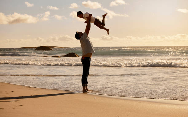 istock Caucasian single father bonding with his son and throwing him up before catching him. Dad playing with son on the beach during the day. Cute little boy enjoying free time with his parent 1398306383