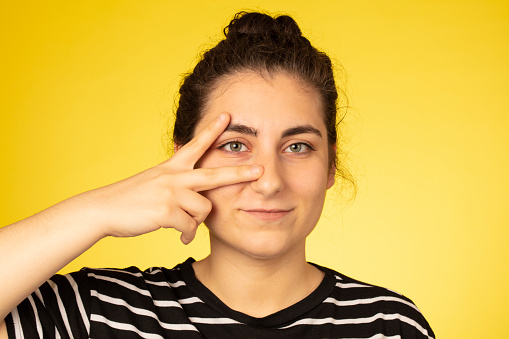 Portrait of smiling woman wearing striped t-shirt showing peace sign on yellow background