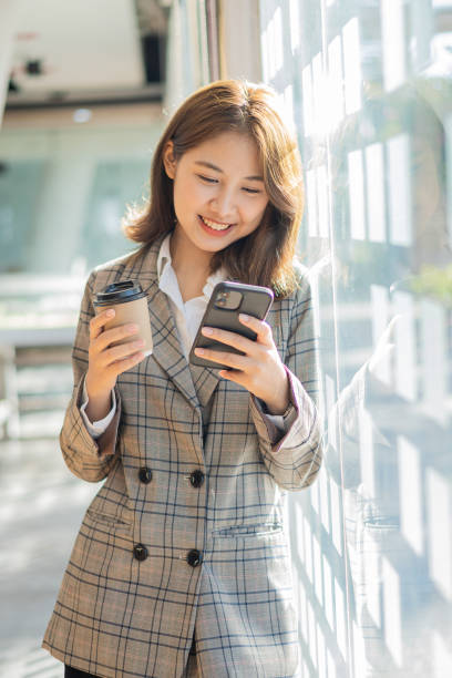 istock Successful young Asian woman talking on mobile phone during break from work. While standing near the copy space of your ad text or promotional material 1398308767