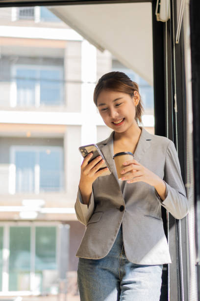 istock Successful young Asian woman talking on mobile phone during break from work. While standing near the copy space of your ad text or promotional material 1398308781