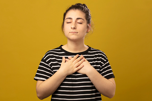 Young woman praying and holding hands in prayer gesture standing in studio. Namaste. Young woman praying in studio.