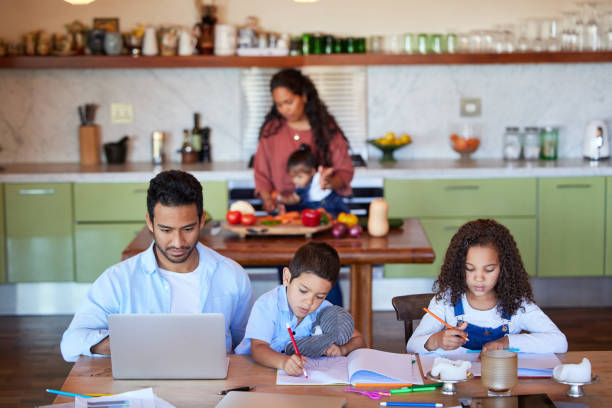 istock Young dad working on laptop while kids draw and do homework. Father and two children working and drawing at table while mom is busy in kitchen during coronavirus pandemic 1398310248