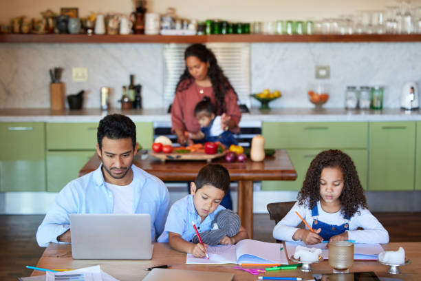 istock Family working at a kitchen table, doing homework at home. A young man using a laptop next to his children. A little boy and girl playing while their father is online. Remote learning in quarantine 1398310694