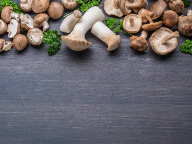 istock Different brown colored edible mushrooms on black table with herbs. Top view. 1398310960