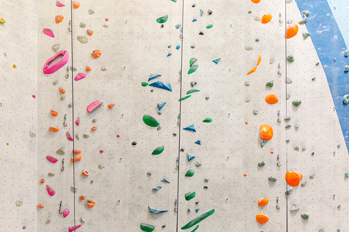 Stock photo of a white rock climbing wall. The grips on it are colorful. There are nobody on the photo.
