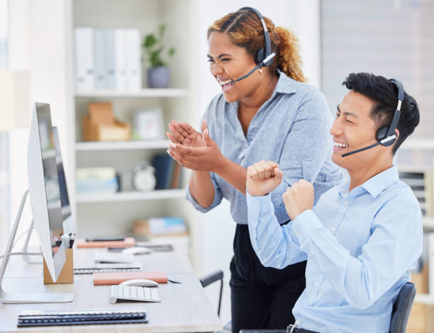 istock Two happy young diverse call centre telemarketing agents clapping and cheering with joy while working together in an office. Excited african american and asian assistants celebrating successful sales and reaching targets to win 1398313323