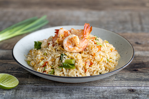 Thai fried rice with shrimp, green onion, lime on wooden background, side view. Traditional Thai street food.