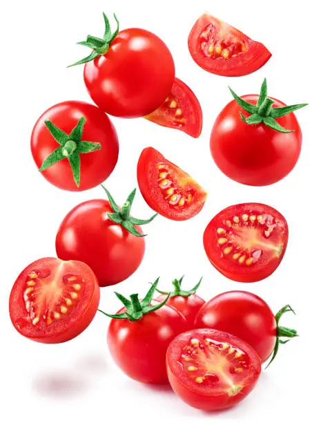 Photo of Falling cherry tomatoes and tomato slices isolated on white background. Macro shot. Popular worldwide product as ingredient in many mediterranean dishes.
