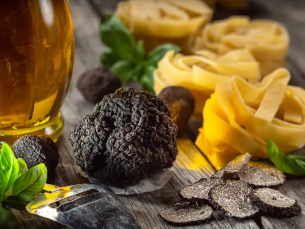 Photo of Black edible winter truffle, tagliatelle and fresh basil on wooden table. The most popular cooking ingredients.