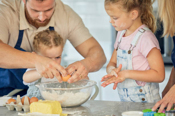 istock Caucasian father helping little daughter crack an egg into a bowl while baking in the kitchen at home. Family being messy and having fun while preparing ingredients for cake batter or cookie dough 1398319686