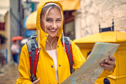 Young girl with a yellow raincoat and map on the street while enjoying a walk through the city on a rainy day.