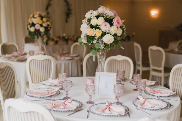 Table setting at the wedding reception. Floral compositions with beautiful flowers and greenery, candles, laying and plates on a decorated table.