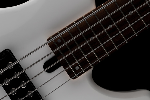 Close-up picture of a white, 5 strings bass guitar with pickup and fretboard on a black background