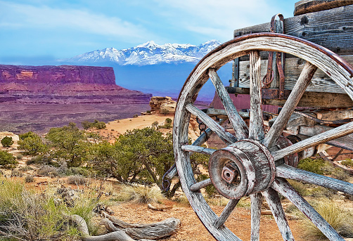 rustic wood wagon in foreground, close view of front wheel, snowcapped mountains in background, blue sky, no people