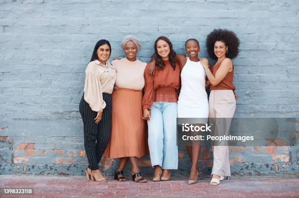 Group Of Five Young Happy Cheerful Businesswomen Hugging While Standing Against A Wall Outside In The City Portrait Of Happy Colleagues Holding Hands And Smiling Standing In A Line Outdoors Stock Photo - Download Image Now