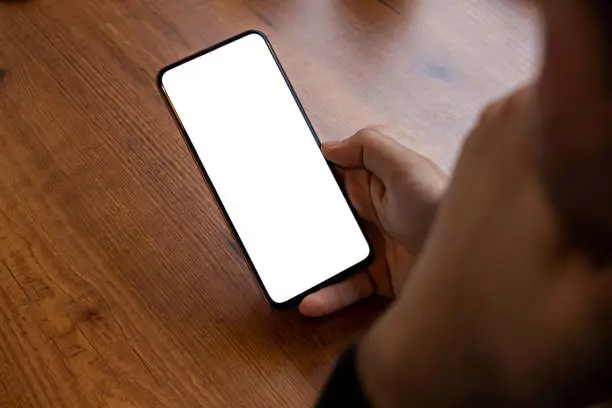 Mockup image of a man holding smartphone with blank white screen while sitting in a cafe. Mobile phone in hand with copy