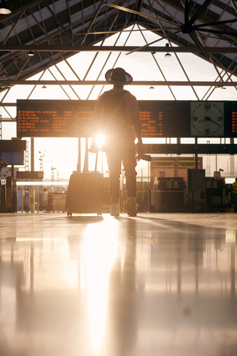 Silhouette of a man wearing a hat and carrying a suitcase looking at a destination travel panel